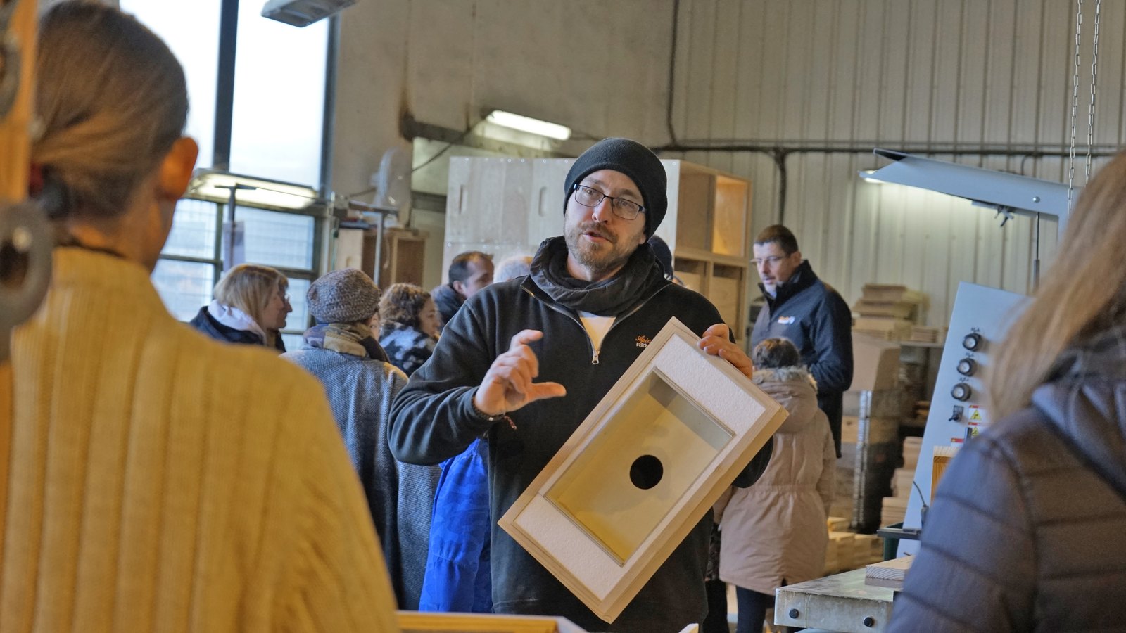 Un membre de l’équipe présente un élément de ruche aux visiteurs dans l’atelier de menuiserie lors des portes ouvertes 2024