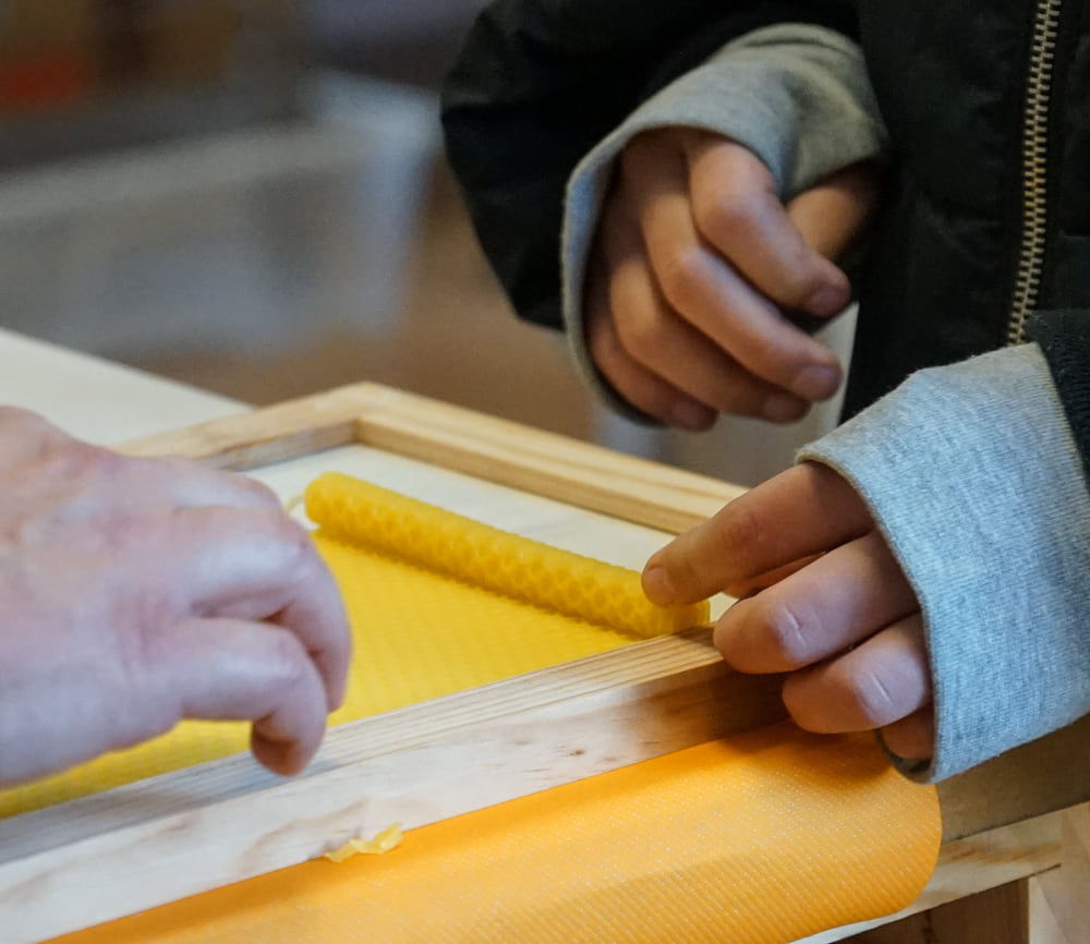Des mains roulent une feuille de cire pour fabriquer une bougie